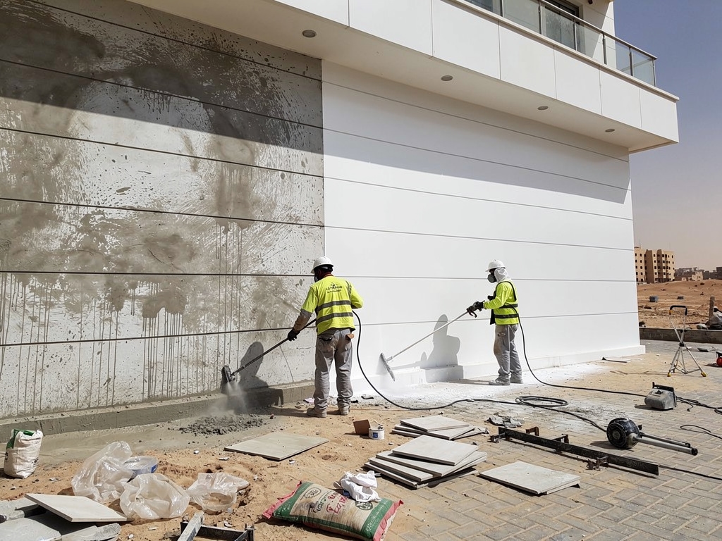 Workers performing post-construction exterior cleanup on a newly built development in Giza